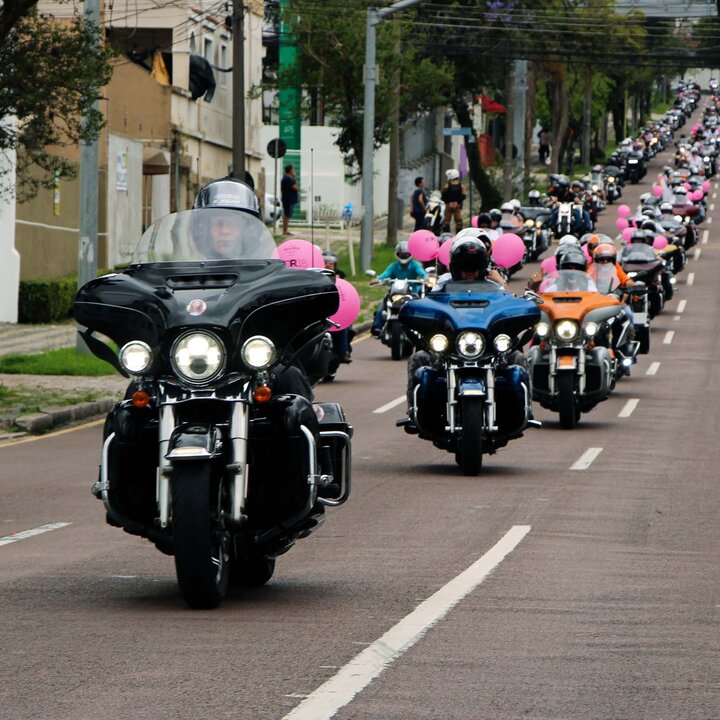 Fila de motos Harley-Davidson numa avenida de Curitiba, com balões cor-de-rosa do Hard Rock Cafe presos às motos, no desfile do Outubro Rosa