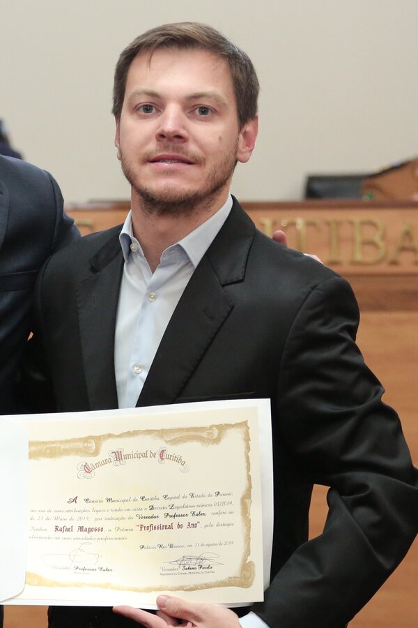 Rafael Magosso, de terno escuro, segura o diploma de Profissional do Ano no plenário da Câmara Municipal de Curitiba